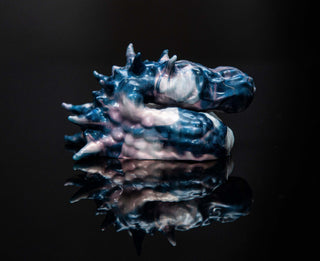 A blue and white Fantasticocks Dracul the Trans Male Packer figurine with a reflection on a black surface, portraying authentic selves.